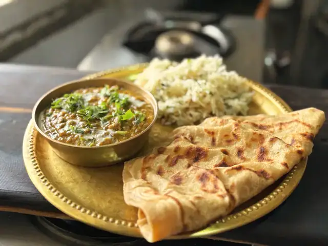 Dal, jeera rice and a stuffed paratha on a brass plate
