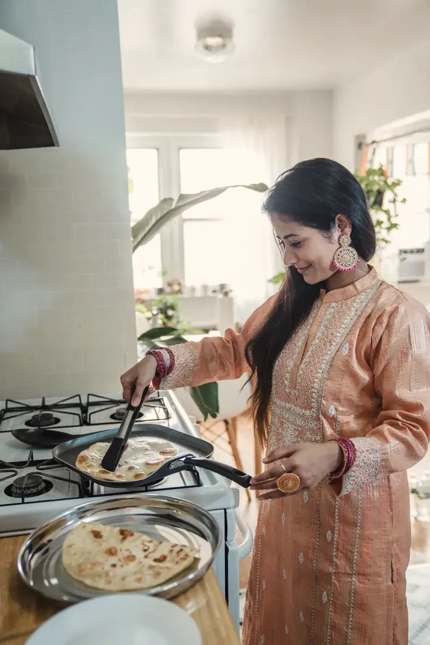 A woman cooking flatbread on the stove in a bright home kitchen