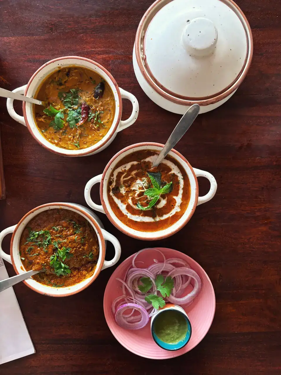 Three bowls of dal with sliced onion and green chutney on the side