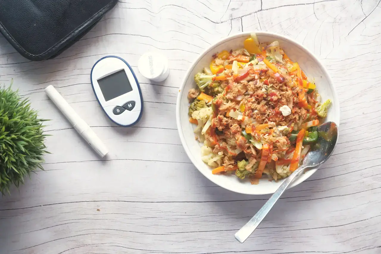 A glucometer beside a bowl of mixed vegetables and grain