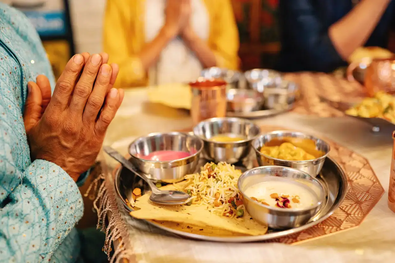 Hands joined in thanks beside a steel thali of home-cooked food