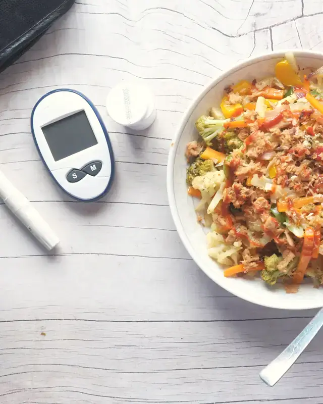 A glucometer beside a bowl of mixed vegetables and grain