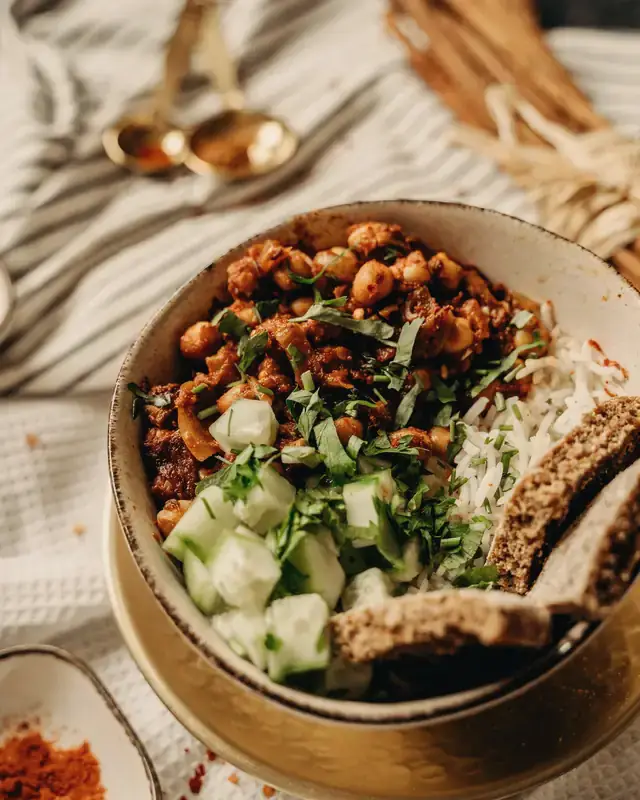 A bowl of chana masala with rice, cucumber and brown bread