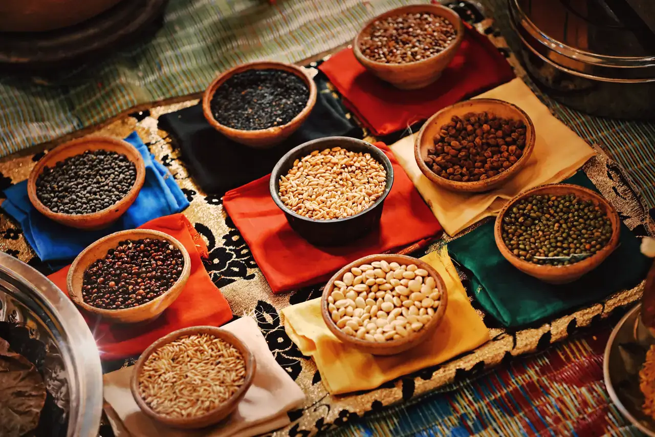 Clay bowls of whole grains, millets and pulses laid out on coloured cloth