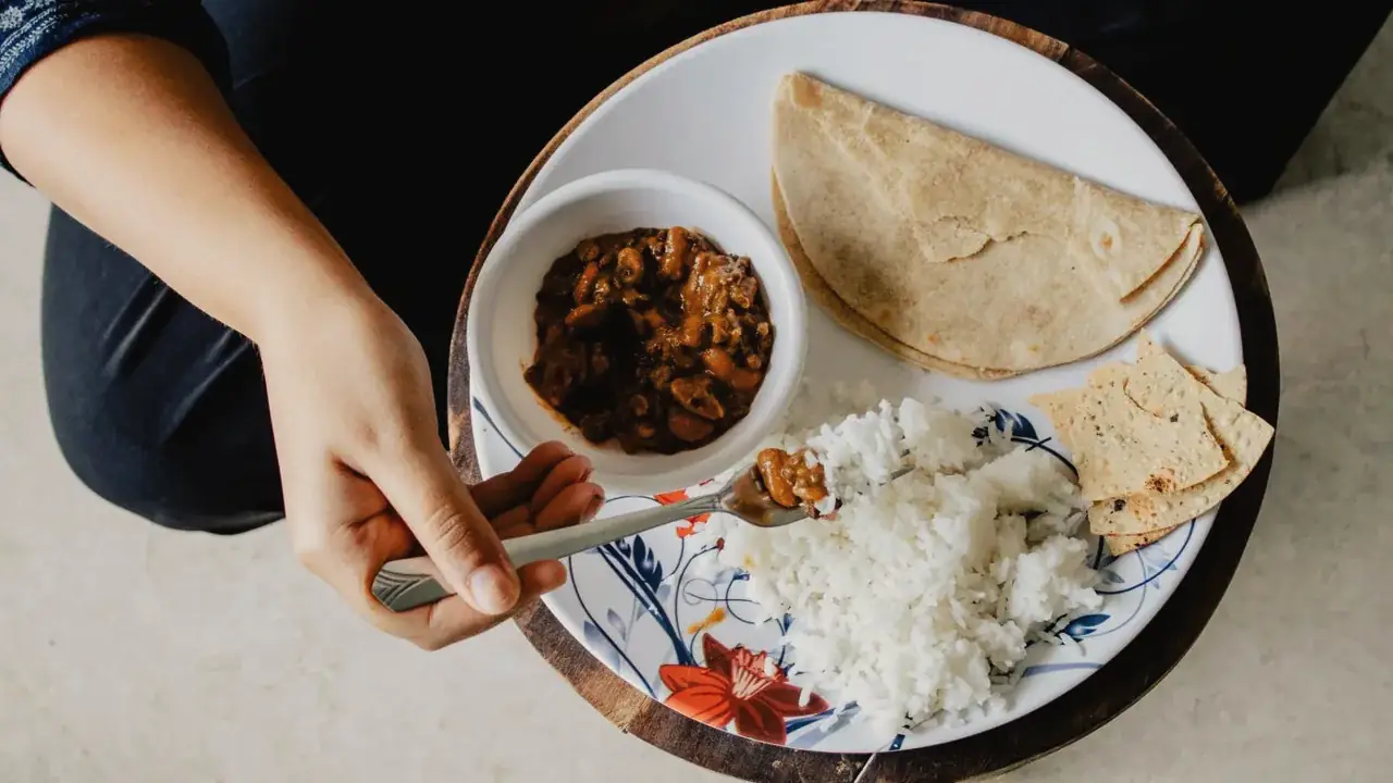 Roti, rice, dal and papad on a plate, being eaten