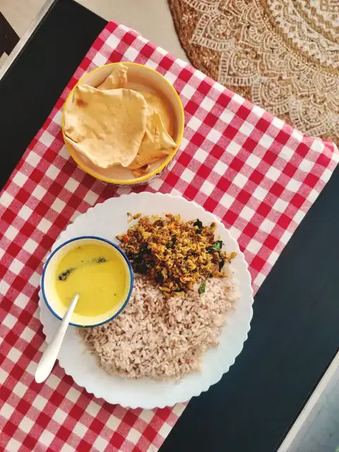 A home-style plate with dal, a vegetable stir-fry, rice and papad on a red checked cloth