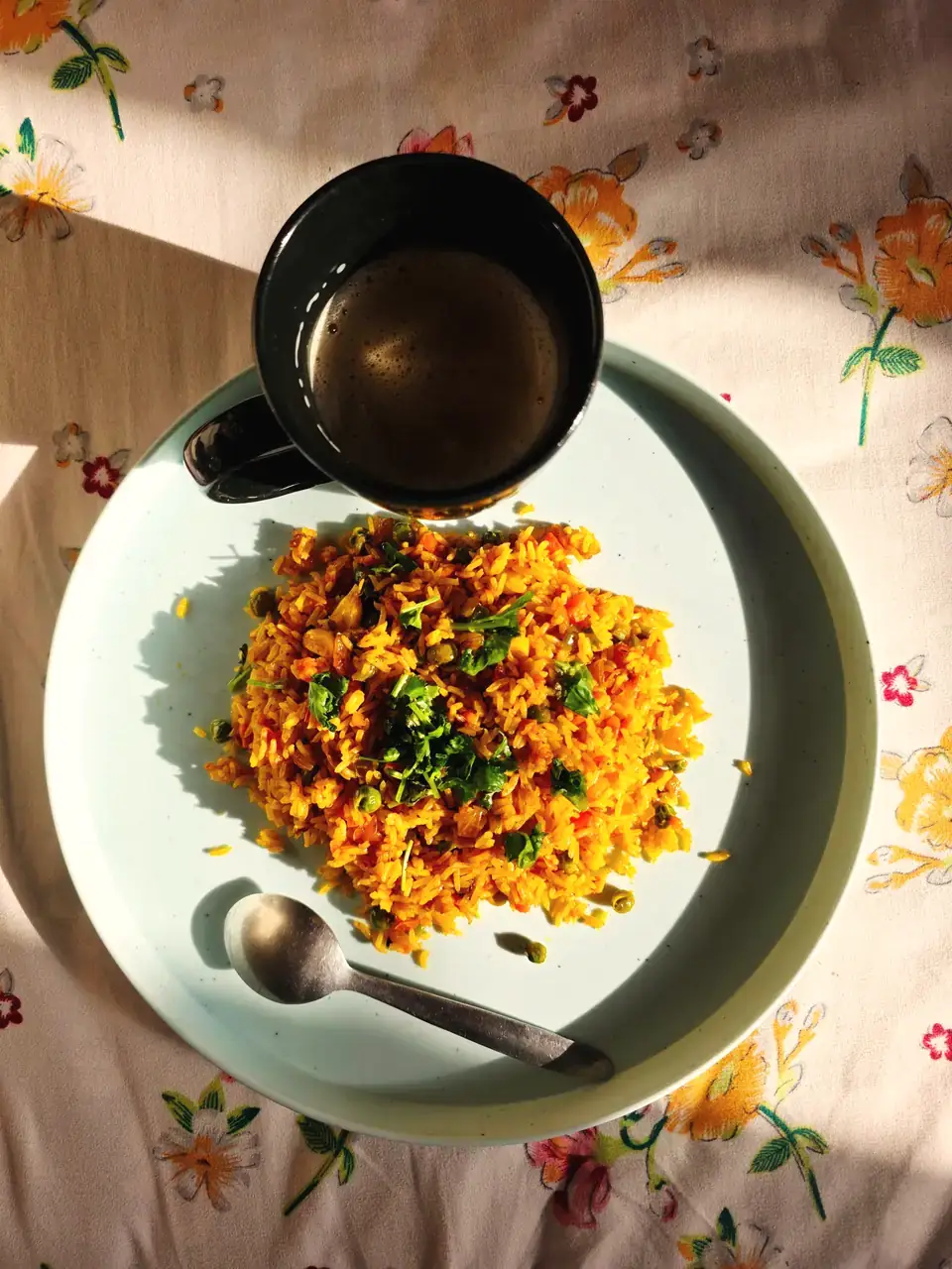 A comforting plate of vegetable pulao beside a cup of tea on a floral tablecloth