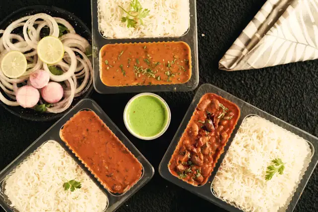 Packed lunch trays of dal, rajma and rice with green chutney, ready for delivery